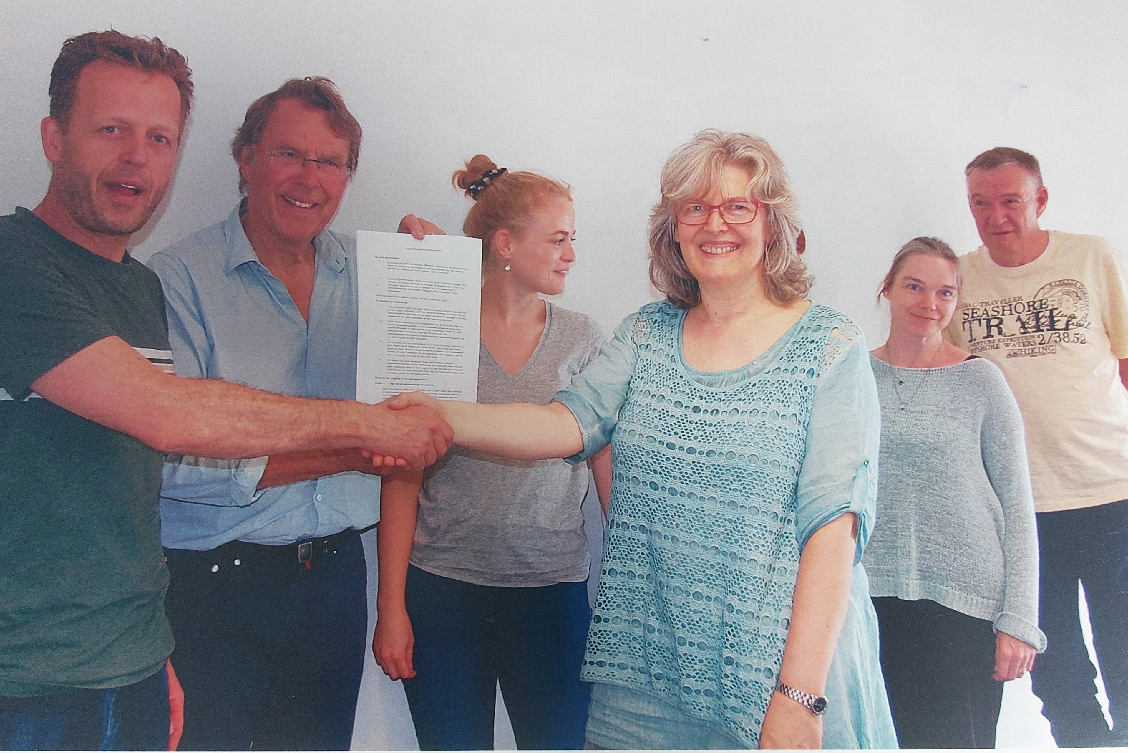 Brigitte schudt de hand van een man. Vincent houdt de statuten van Quiet omhoog. Stephanie en twee andere mensen kijken toe.